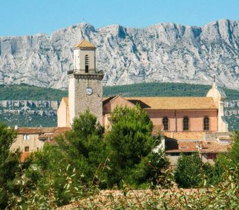 Église de pierre ocre au pied de falaises calcaires blanches sous ciel bleu méditerranéen.