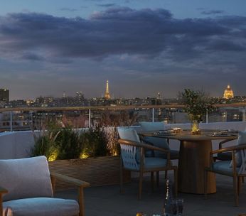 Terrasse moderne en soirée surplombant une rivière urbaine illuminée, avec mobilier contemporain et éclairage ambiant.