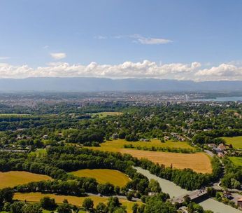 Paysage aérien de vallée verdoyante avec champs jaunes, rivière sinueuse et villages sous ciel nuageux.
