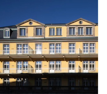 Façade jaune d'un immeuble classique aux fenêtres régulières et toit mansardé, ciel bleu en arrière-plan.