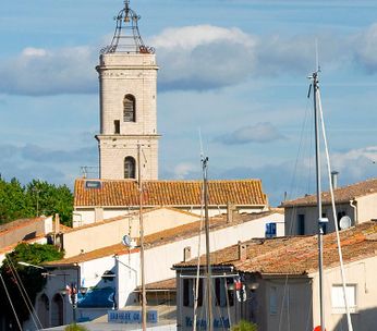 Port méditerranéen avec bateaux amarrés, église au campanile doré et bâtiments colorés sous ciel bleu.