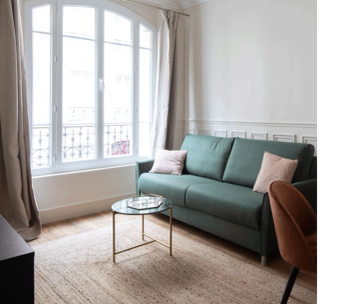 Salon minimaliste avec canapé vert, fauteuil marron, table basse et large baie vitrée.