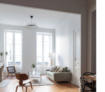 Intérieur minimaliste avec portes-fenêtres blanches, fauteuil beige et mobilier discret sous lumière naturelle.