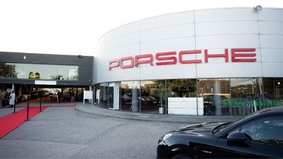 Façade d'une concession automobile Porsche avec parking et voitures exposées.
