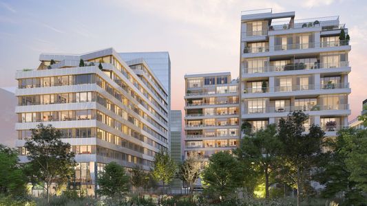 Immeubles résidentiels modernes aux façades claires, entourés de verdure, sous un ciel nuageux.