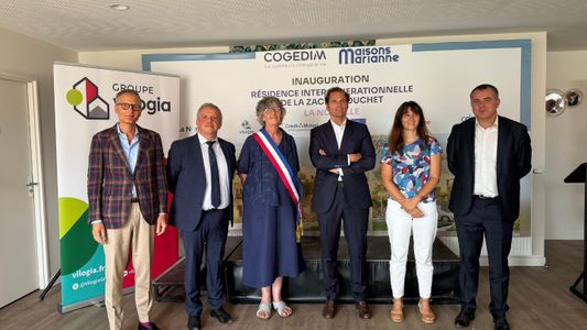 Groupe de neuf personnes en tenue formelle posant ensemble dans un bureau moderne.