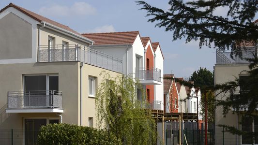 Rangée de maisons résidentielles colorées avec jardins sous un ciel nuageux.