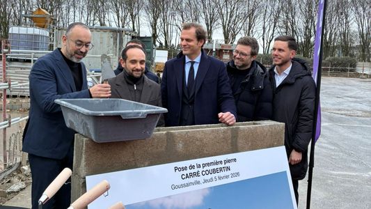 Cinq hommes en costumes tenant les plans d'un projet de construction dans un parc.