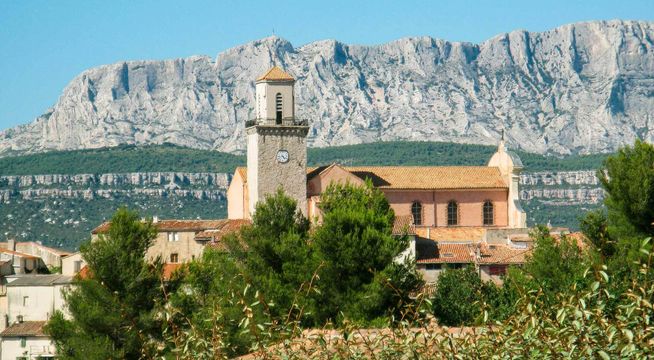 Église de pierre ocre au pied de falaises calcaires blanches, paysage méditerranéen.