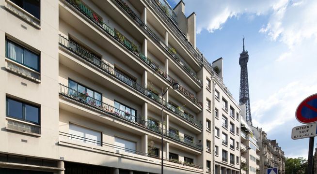 Immeuble parisien hausmannien avec la Tour Eiffel en arrière-plan par temps nuageux.