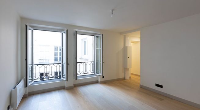 Pièce vide aux murs blancs avec porte-fenêtre donnant sur balcon et alcôve éclairée.