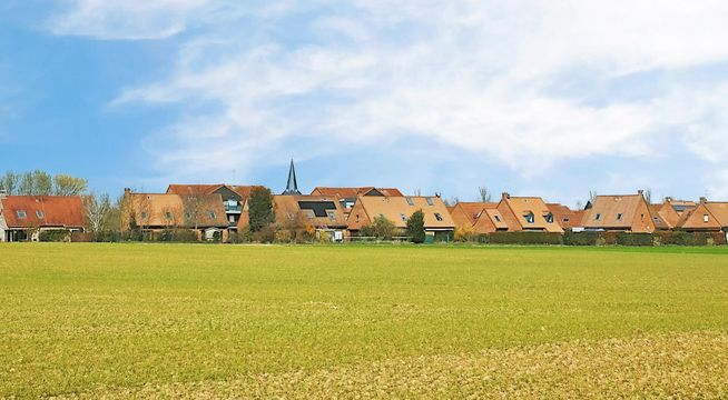 Petit village aux maisons colorées au bord d'un vaste champ vert sous ciel dégagé.
