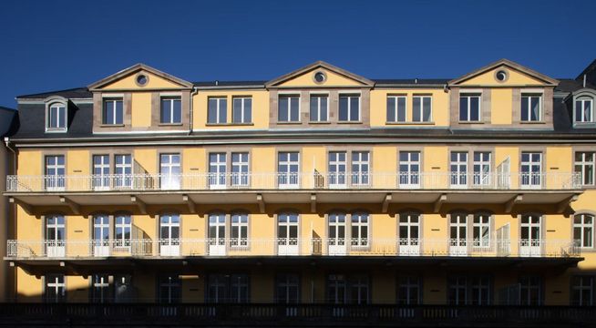 Immeuble de style haussmannien aux façade jaune pâle et toiture mansardée sous ciel bleu.