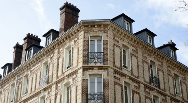 Immeuble haussmannien parisien avec façade ornée, mansardes et cheminées, sous ciel nuageux.