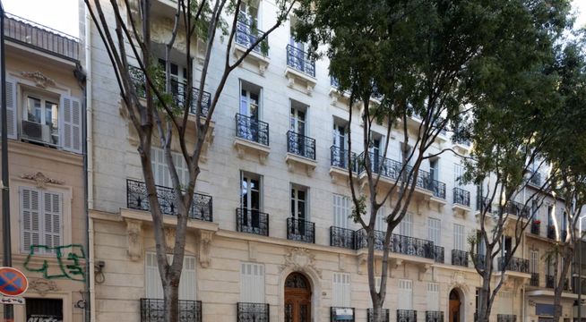 Immeuble haussmannien parisien avec façade beige, fenêtres régulières et arbres devant.