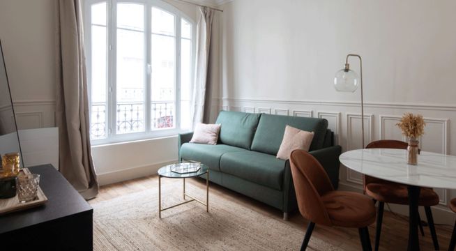 Petit salon lumineux avec canapé vert sapin, fauteuil marron, table basse et baies vitrées.