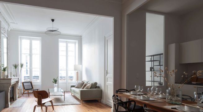 Salon moderne avec portes-fenêtres blanches donnant sur un balcon, murs gris clair et mobilier minimaliste.