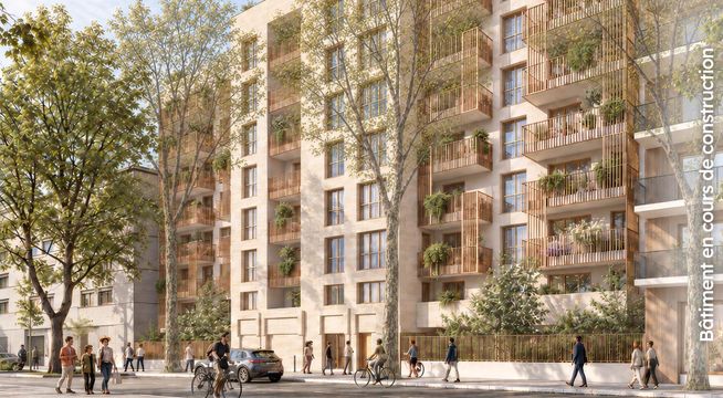 Immeuble résidentiel moderne de plusieurs étages en brique beige et rose, avec arbres et piétons sur le trottoir.