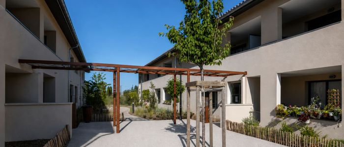 Cour intérieure avec bâtiments modernes, arbres et pavage ensoleillé sous ciel bleu.