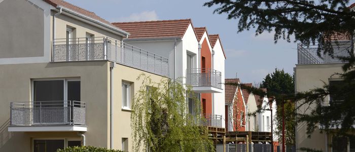 Rangée de maisons résidentielles colorées avec jardins sous un ciel nuageux.